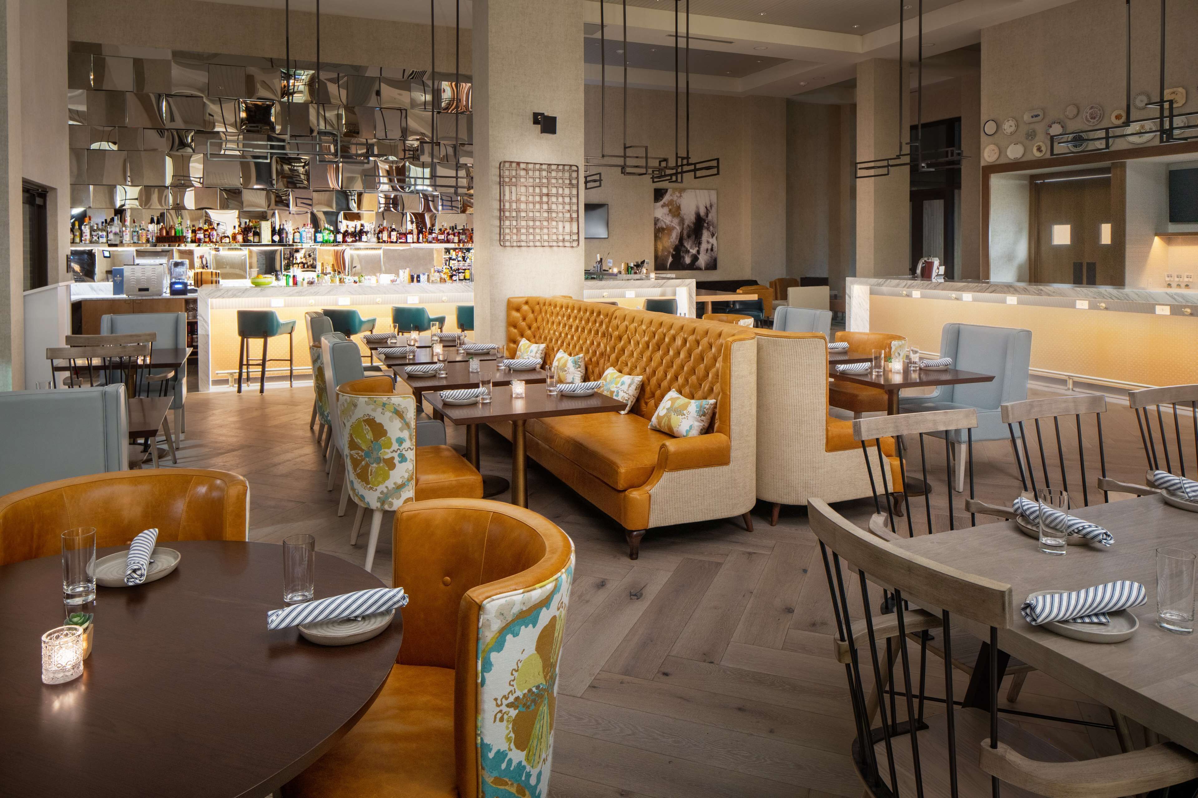 Un hall d’hôtel moderne avec un bar, des espaces aménagés pour s’asseoir et une cuisine en arrière-plan.