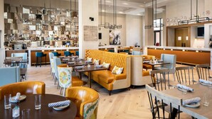 Een modern restaurant met hoge plafonds, hanglampen en een mix aan zitplaatsen, waaronder tafels en een bank.