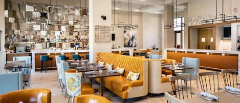 En moderne restaurant med højt til loftet, hængende lamper og varieret siddeplads med borde og en sofa.