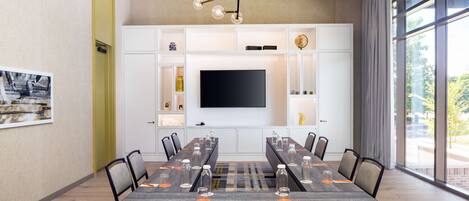 A conference room with a long table, chairs, a television, and storage cabinets.