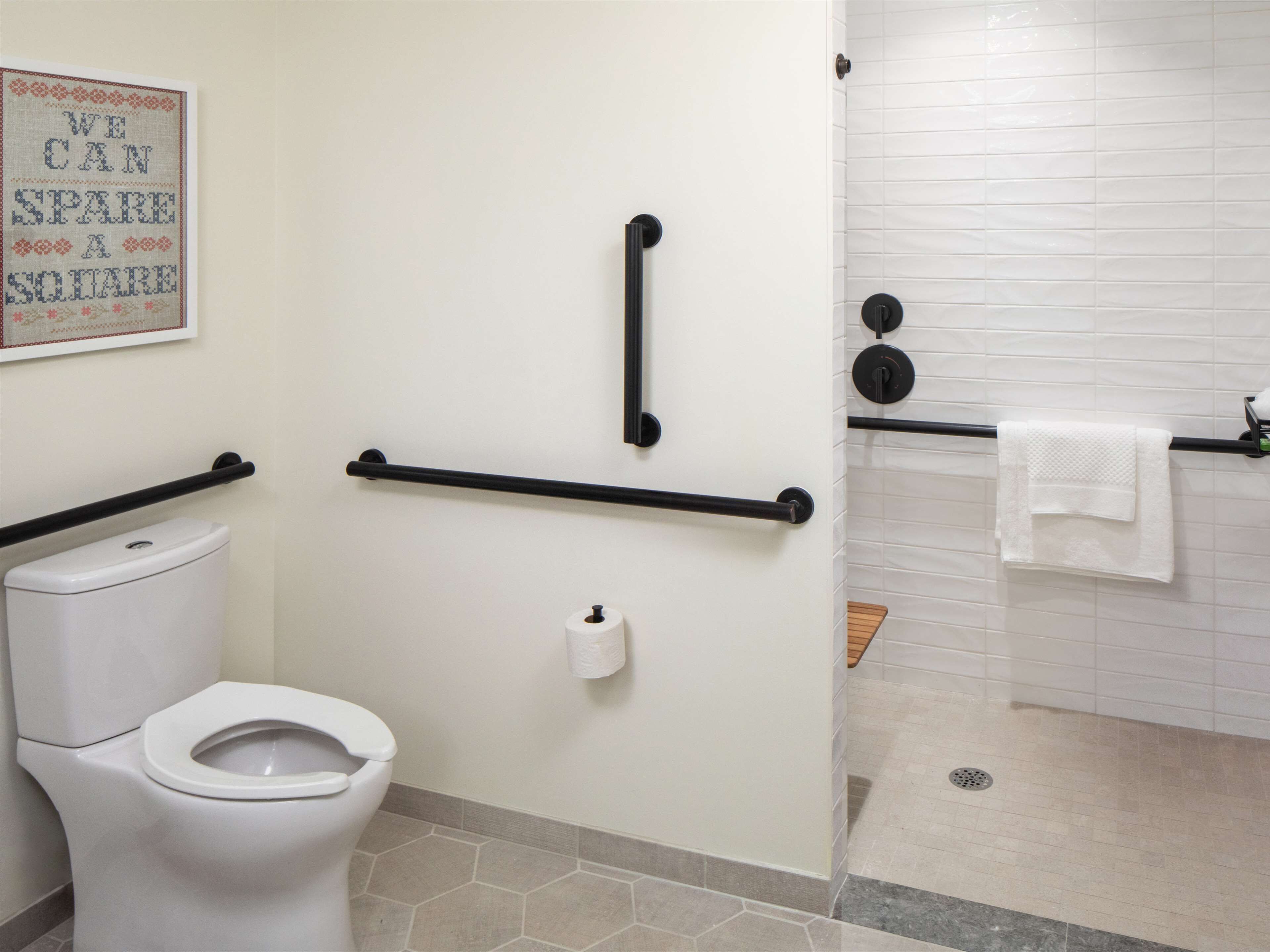 Un baño con inodoro, barras de apoyo, toallero y zona de ducha.