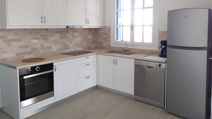 A kitchen with white cabinets, a stainless steel oven, a dishwasher, and a refrigerator. - La Maison Bleu (Messini)