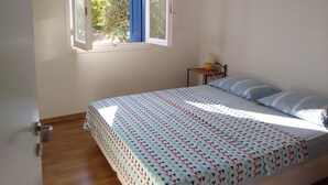 A bedroom with a bed, a window, and a nightstand with a lamp. - La Maison Bleu (Messini)