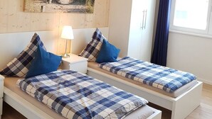Quarto com duas camas, uma mesa de cabeceira, abajur, guarda-roupa e um quadro na parede.