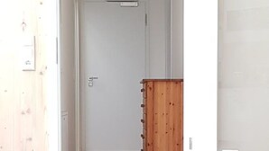 Um corredor com um aparador de madeira, uma porta e um chão de azulejos claros.