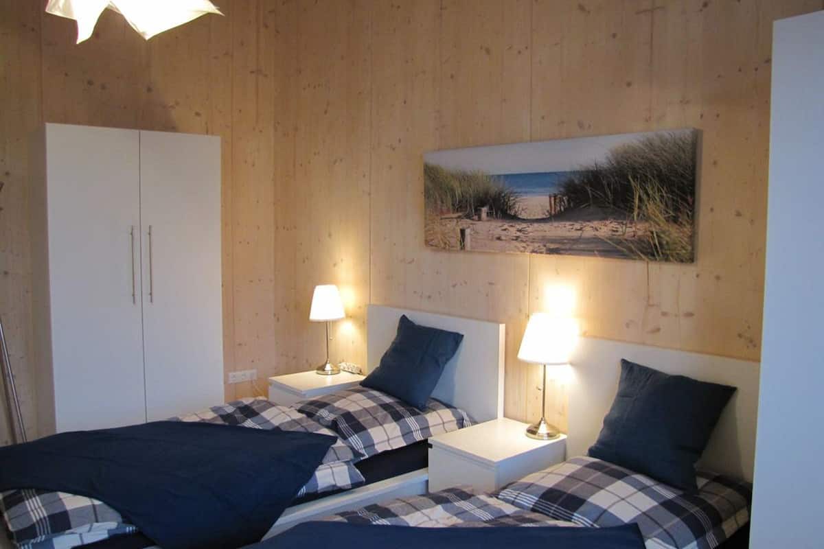 Ein Zimmer mit zwei Betten, jeweils mit Nachttisch und Lampe. Es gibt einen Kleiderschrank und ein Bild an der Wand.