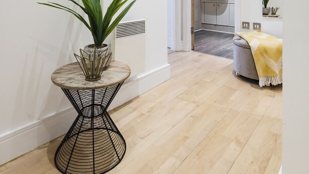 Un couloir avec une table ronde, une plante en pot, une horloge murale et une porte donnant sur une salle de bain.