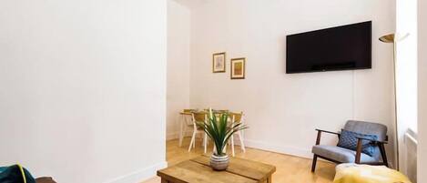 A living room with a wooden coffee table, a TV mounted on the wall, a sofa, and a chair.