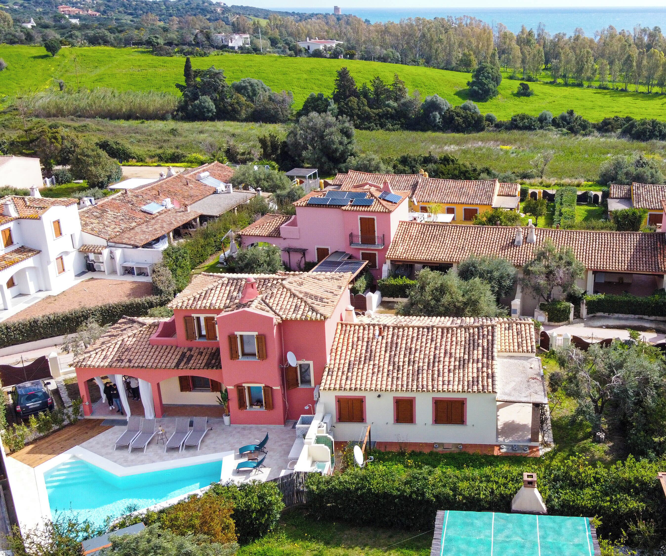 A residential area with houses featuring red-tiled roofs, a swimming pool, and a view of the sea.