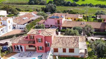 A residential area with houses featuring red-tiled roofs, a swimming pool, and a view of the sea.