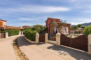A gated residential area with a paved driveway leading to a building with a tiled roof.