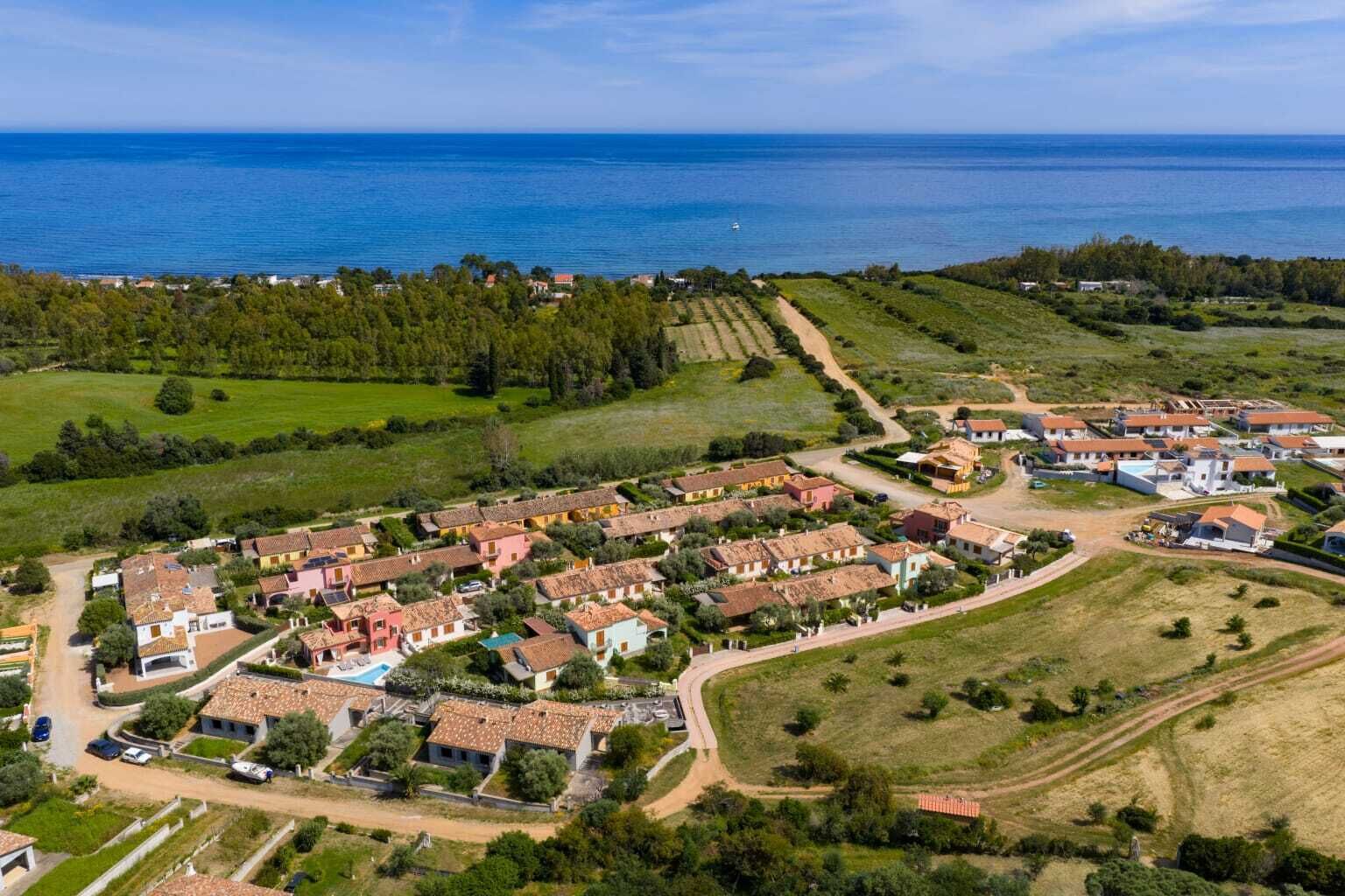 An aerial view of a coastal village with terraced fields, houses with red-tiled roofs, and a clear view of the sea.