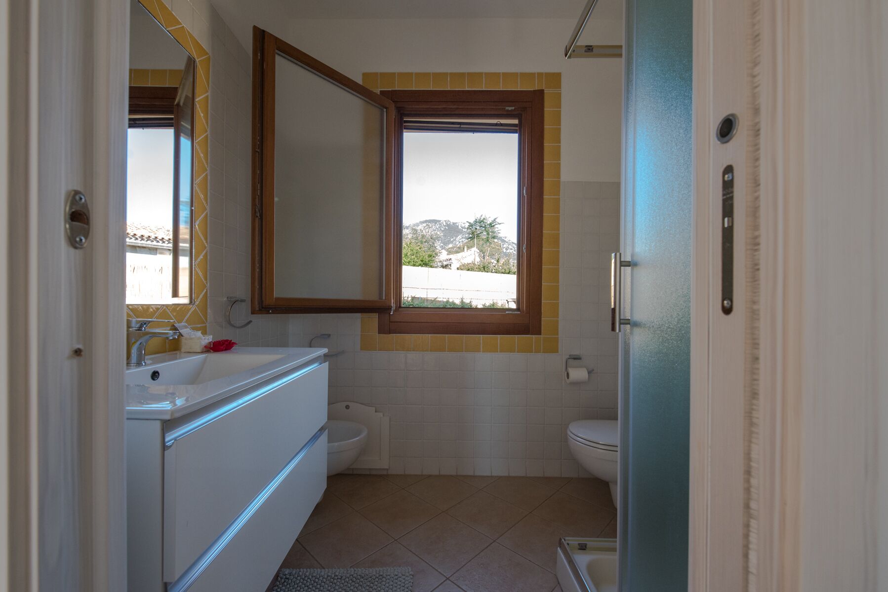 Een badkamer met een wastafel, spiegel, toilet en raam.