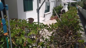 Un bâtiment blanc avec des volets verts, un parasol blanc et des plantes en pot.