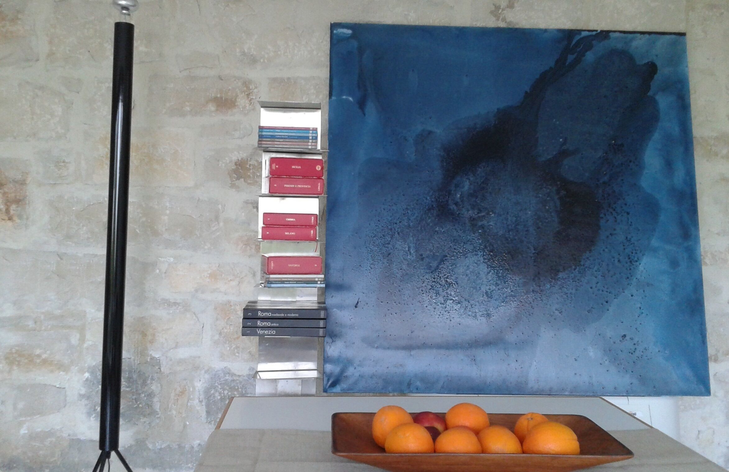 Una habitación con pared de piedra, un cuadro, una pila de libros y una bandeja de madera con naranjas.