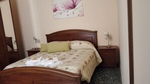 Ein ordentlich bezogenes Bett mit Blumendecke, zwei Nachttische mit Lampen und ein an der Wand hängendes Blumenbild.