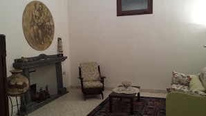 Ein Wohnzimmer mit Kamin, einem Sessel, einer Couch und einem Gemälde an der Wand.