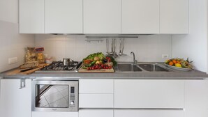 Et moderne køkken med hvide skabe, en rustfri stålbordplade, indbygget mikroovn og gasblus.