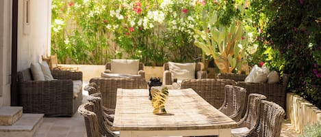 Un patio exterior con mobiliario de mimbre, una mesa y una pérgola que ofrece sombra.