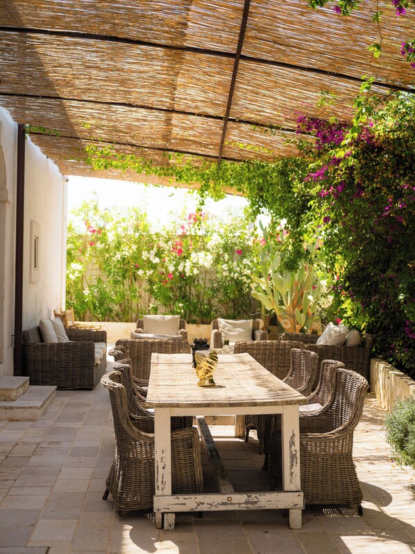 An outdoor patio with wicker furniture, a table, and a pergola providing shade.