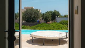 Una piscina esterna con un lettino, immersa nel verde sotto un cielo sereno.