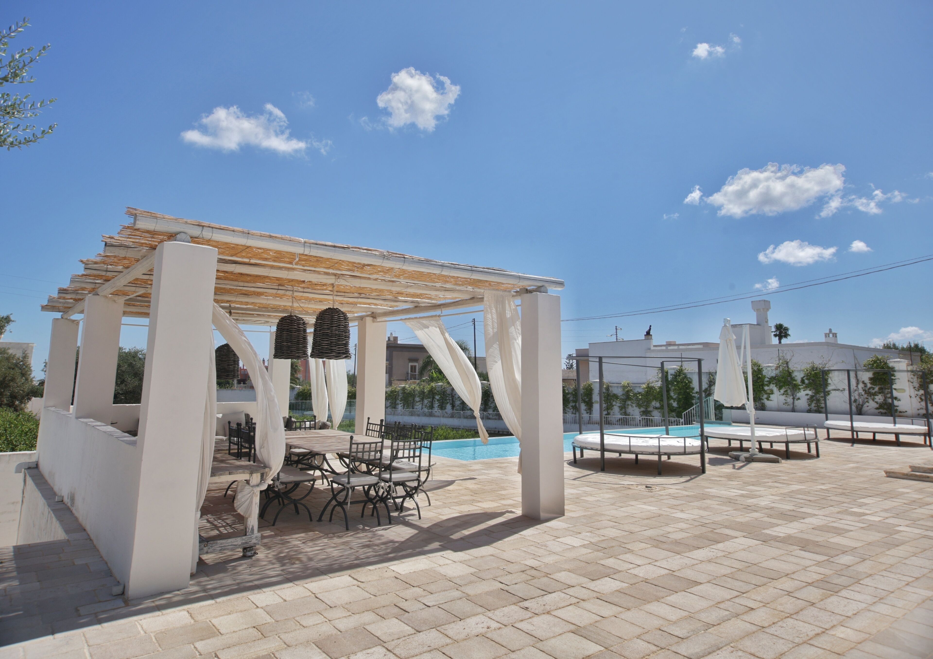 Un espace extérieur avec piscine, agrémenté d’une pergola, de sièges et offrant une vue sur un bâtiment en arrière-plan.