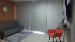 Olohuoneessa on harmaa sohva, punainen tuoli, kuviollinen matto, seinälle asennettu taulutelevisio ja liukuovi.