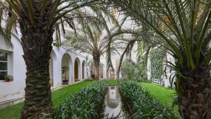 Ein Innenhof mit Palmen, einem zentralen Wasserspiel und bogenförmigen Gängen.