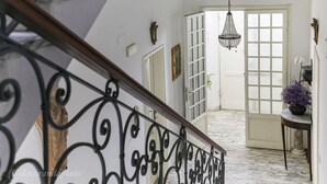 Eine Treppe mit aufwendiger schwarzer Geländerkonstruktion führt zu einem Flur mit Marmorboden, einer weißen Tür und einem hängenden Kristalllüster.