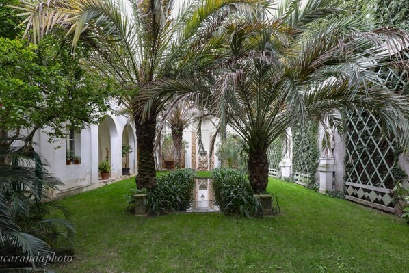 A courtyard with palm trees, a central pathway, and a white building with arches.