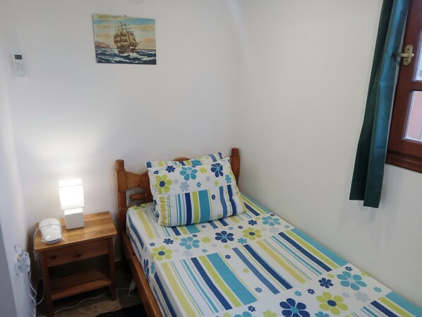 A small bedroom with a single bed, a nightstand, a lamp, and a wall-mounted painting.