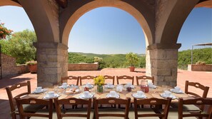 Una mesa redonda dispuesta para comer, con sillas, ubicada en un espacio al aire libre con arcos de piedra y vistas a un paisaje pintoresco.