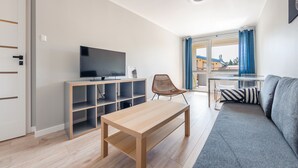A modern living room with a flat-screen TV, a wooden coffee table, a grey sofa, and a dining area with a table and chairs. - Apartamenty Sun & Snow Kopernika (Ustka)