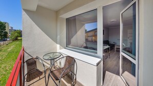 A balcony with wicker chairs, a glass table, and a view of the adjacent room. - Apartamenty Sun & Snow Kopernika (Ustka)