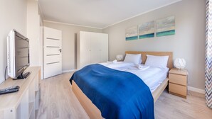 A hotel room with a bed, bedside tables, a TV, and artwork on the wall. - Apartamenty Sun & Snow Kopernika (Ustka)