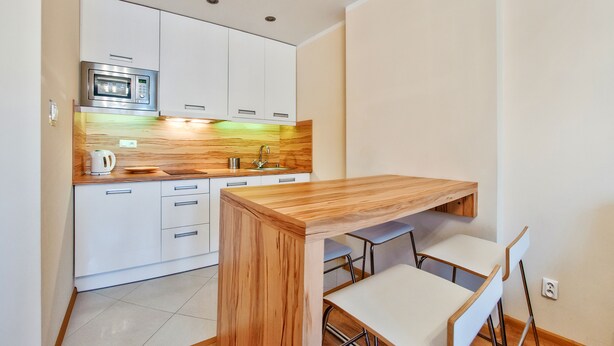 A compact kitchen with white cabinets, a microwave, a sink, and a wooden table with two chairs. - Apartamenty Sun & Snow Kopernika (Ustka)