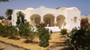 Um edifício branco com três portais em arco e grandes vasos no alpendre.