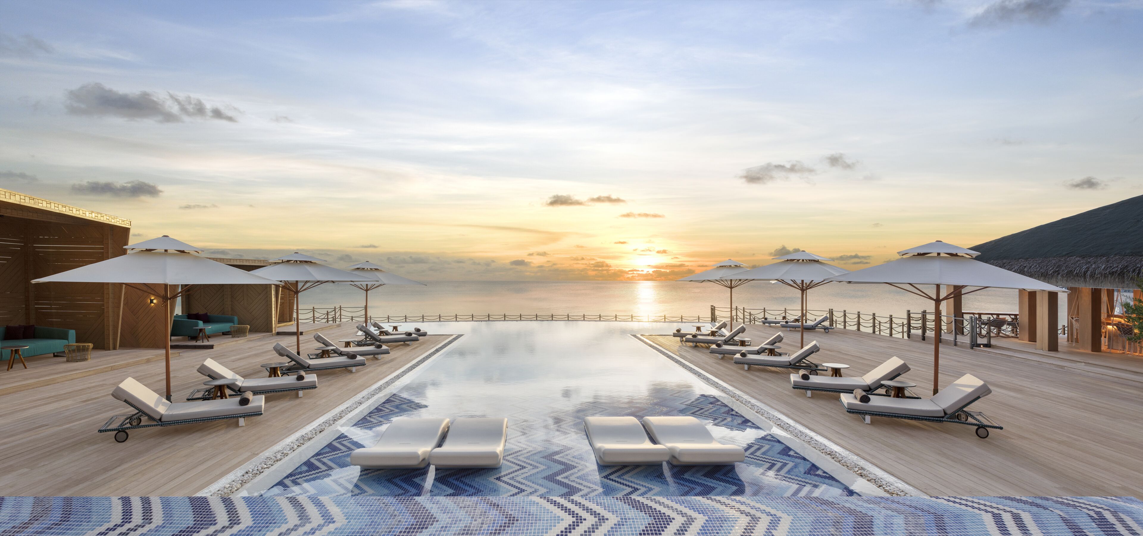 Un espace aménagé au bord de la piscine, avec des chaises longues et des parasols, offrant une vue sur le coucher de soleil sur l’eau.