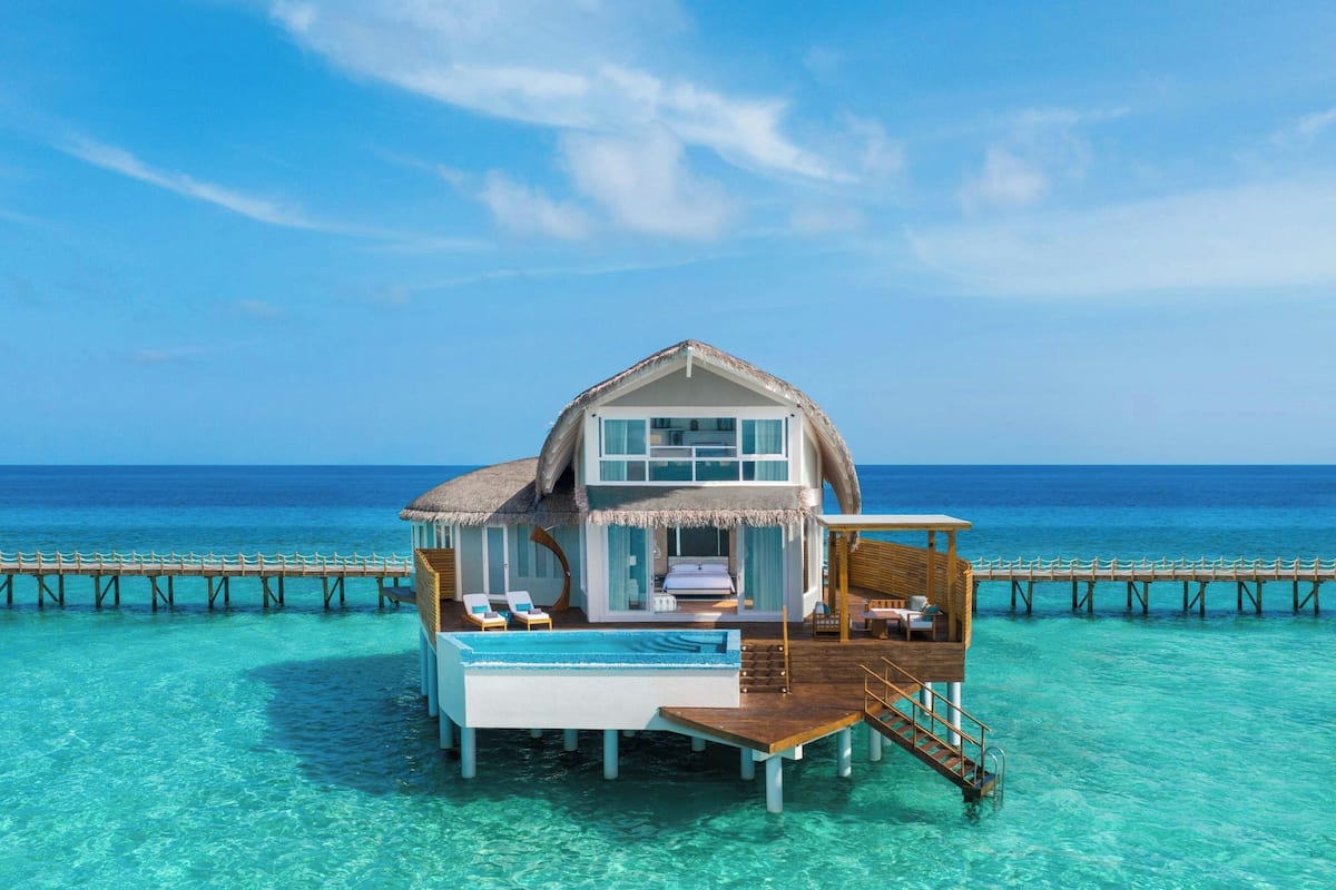 Un bungalow sur pilotis avec un toit de chaume, une piscine et une terrasse en bois.