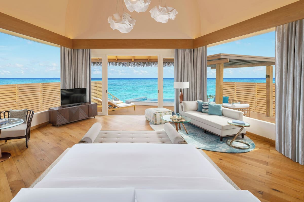 Une chambre spacieuse avec un grand lit, une télévision et un coin salon offrant une vue sur l’océan.