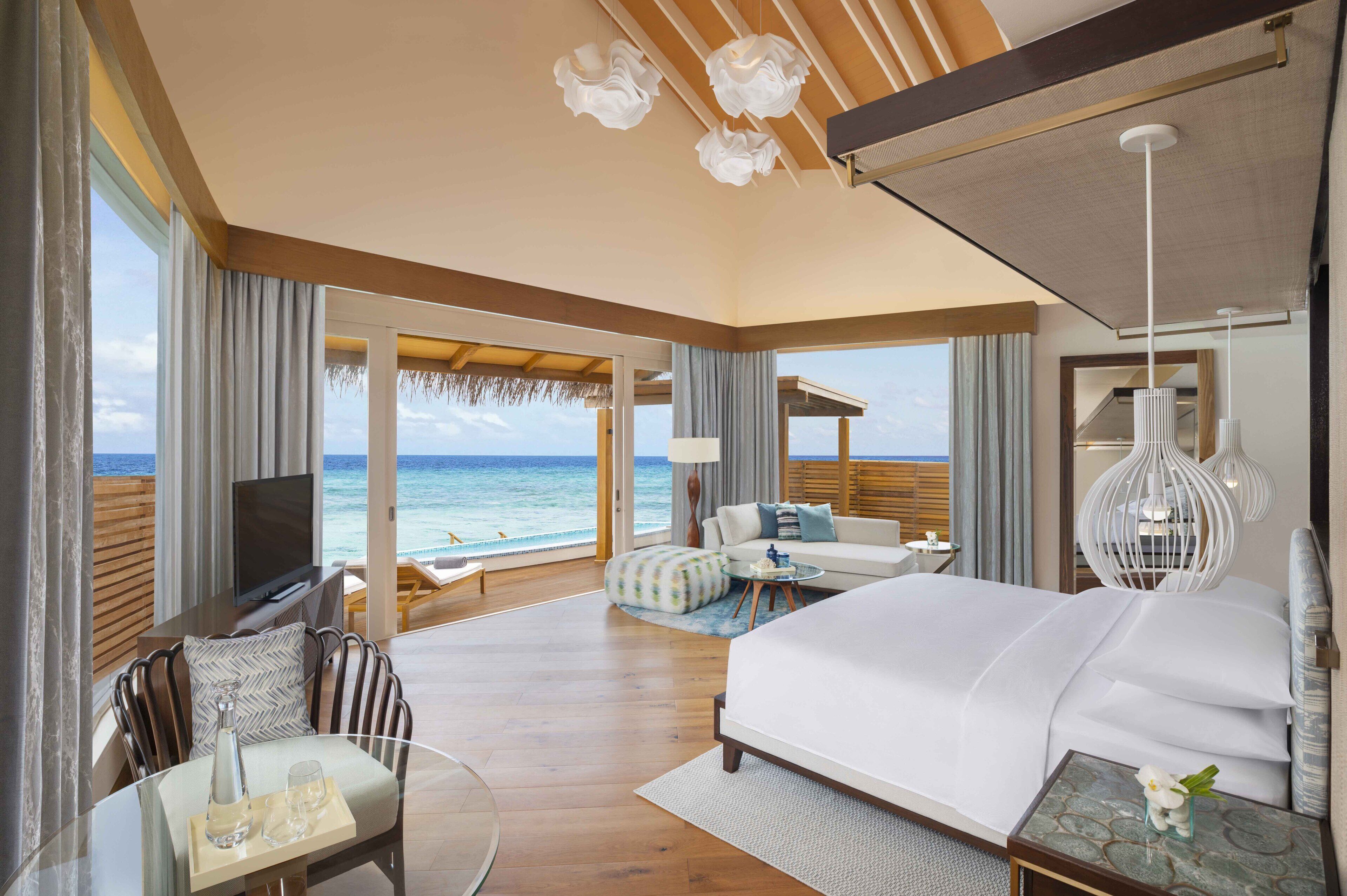 Um quarto espaçoso com uma cama grande, televisão, área de estar com vista para o oceano e uma varanda.