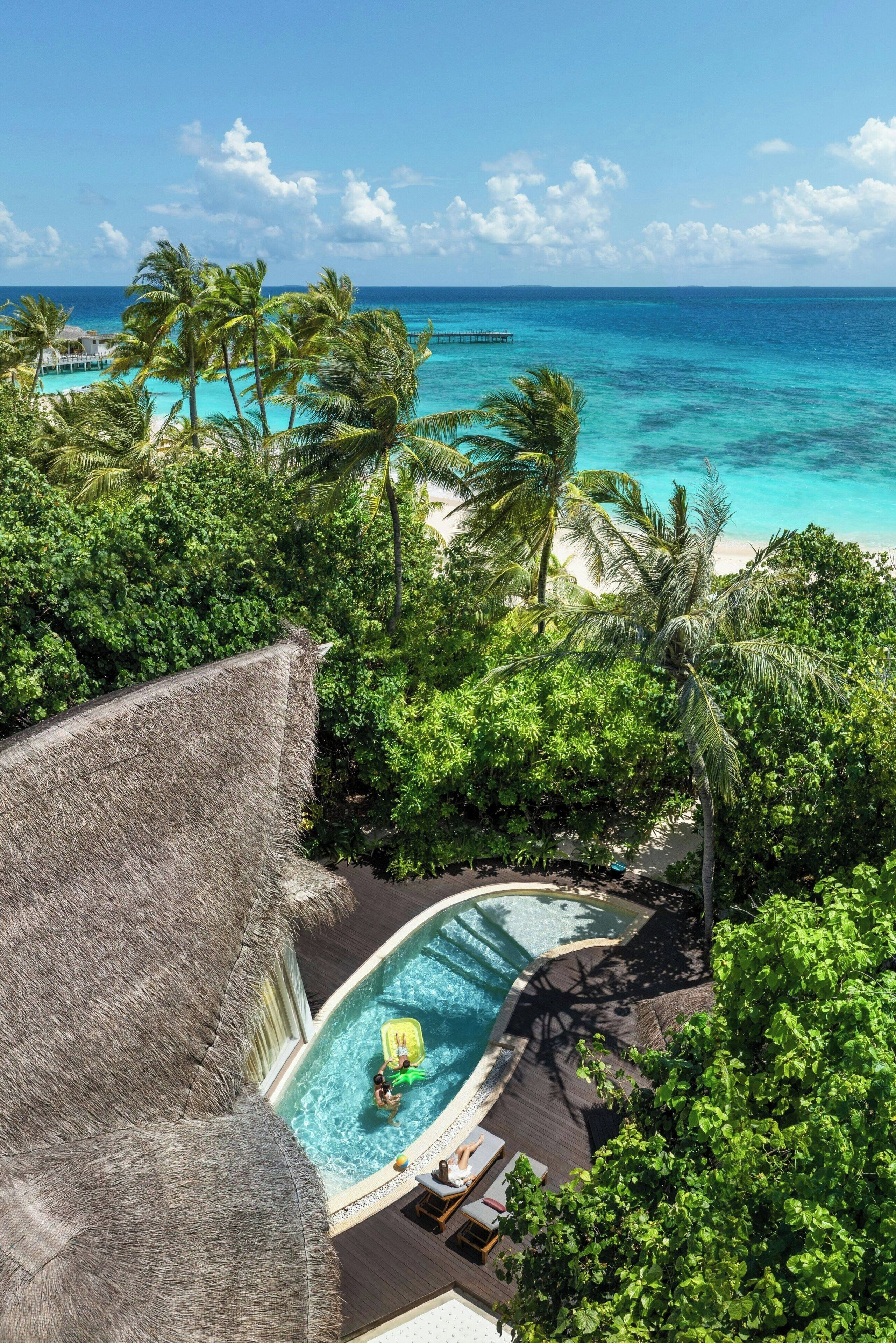 Un resort con piscina rodeada de exuberante vegetación y vista al océano.