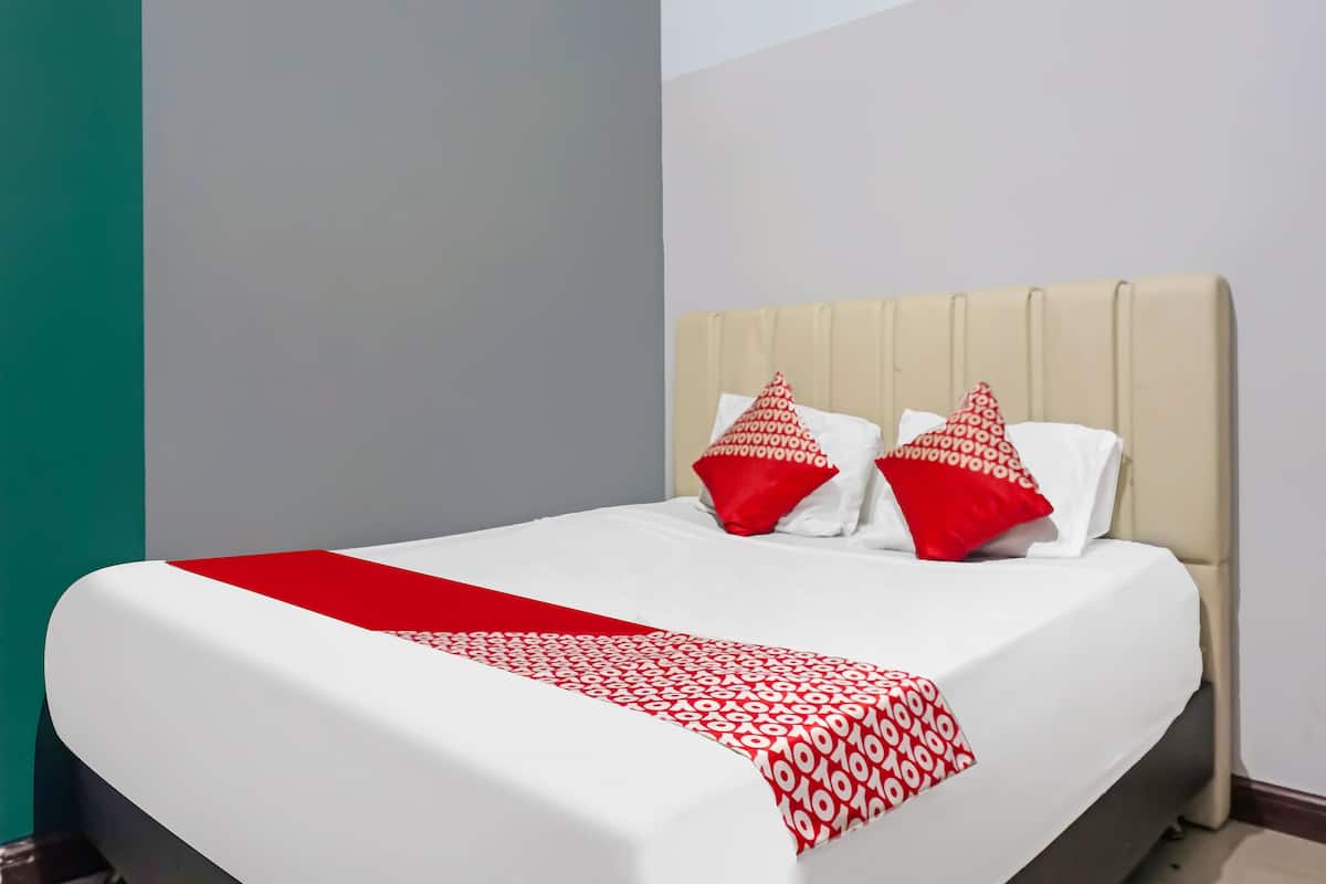 Ein ordentlich bezogenes Bett mit einer weiß-roten Tagesdecke, zwei roten Kissen und einem beige gefärbten Kopfteil.