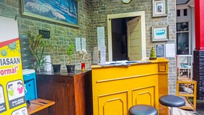 A reception area with a brick wall, a clock, framed pictures, and a yellow counter with stools. - Hotel O Puspita Guesthouse (Bekasi)