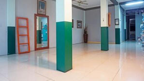A spacious corridor with a polished floor, ceiling fans, and a series of framed pictures on the walls. - Hotel O Puspita Guesthouse (Bekasi)