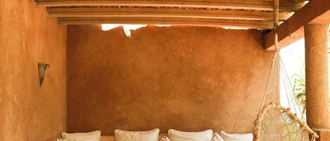 A cozy room with a woven ceiling, a cushioned sofa with patterned pillows, a hanging chair, and a tiled floor.