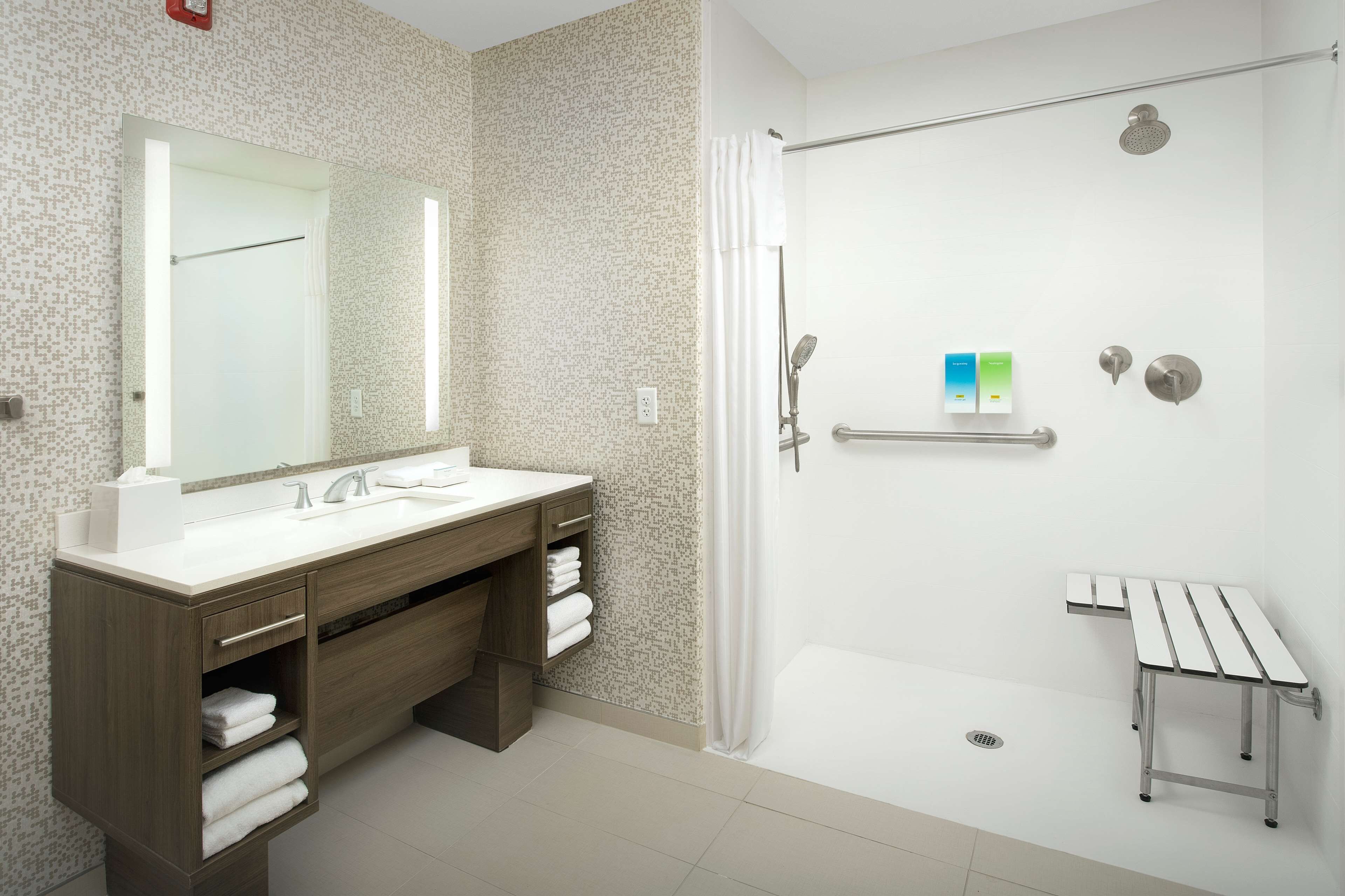 Un baño moderno con un espejo grande, lavamanos dobles, ducha con cabezal de ducha manual y un pequeño banco.