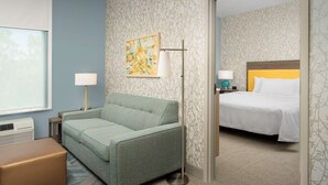 Habitación de hotel con sofá, mesita de noche con lámpara, cama con cabecero y pared con papel tapiz estampado.