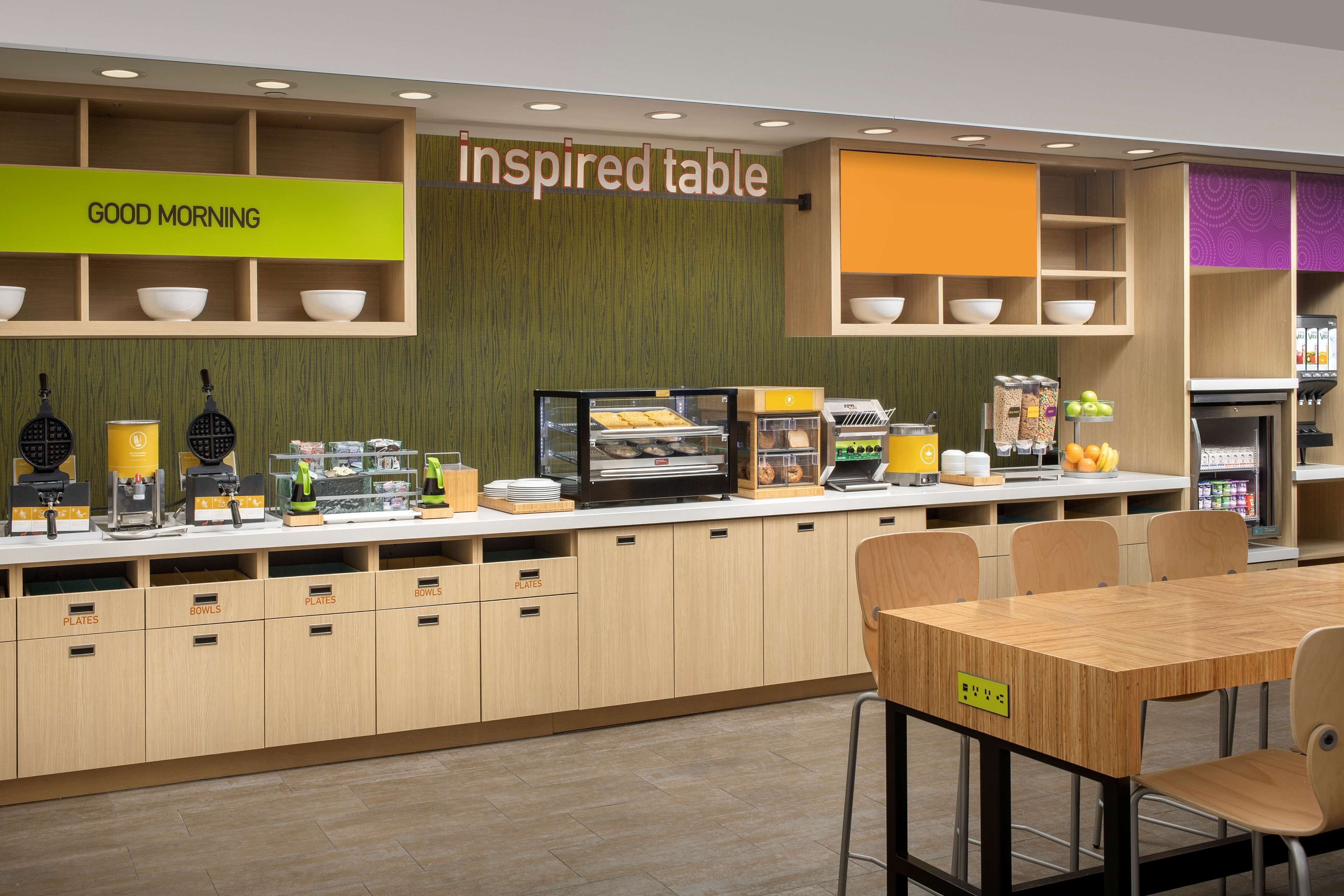 A breakfast area with a self-service station, a table with chairs, and a sign that reads "inspired table".