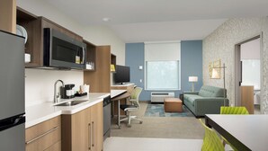Una cocina moderna con microondas, estufa y lavabo, un comedor con mesa y sillas, y una sala de estar con sofá y televisor.